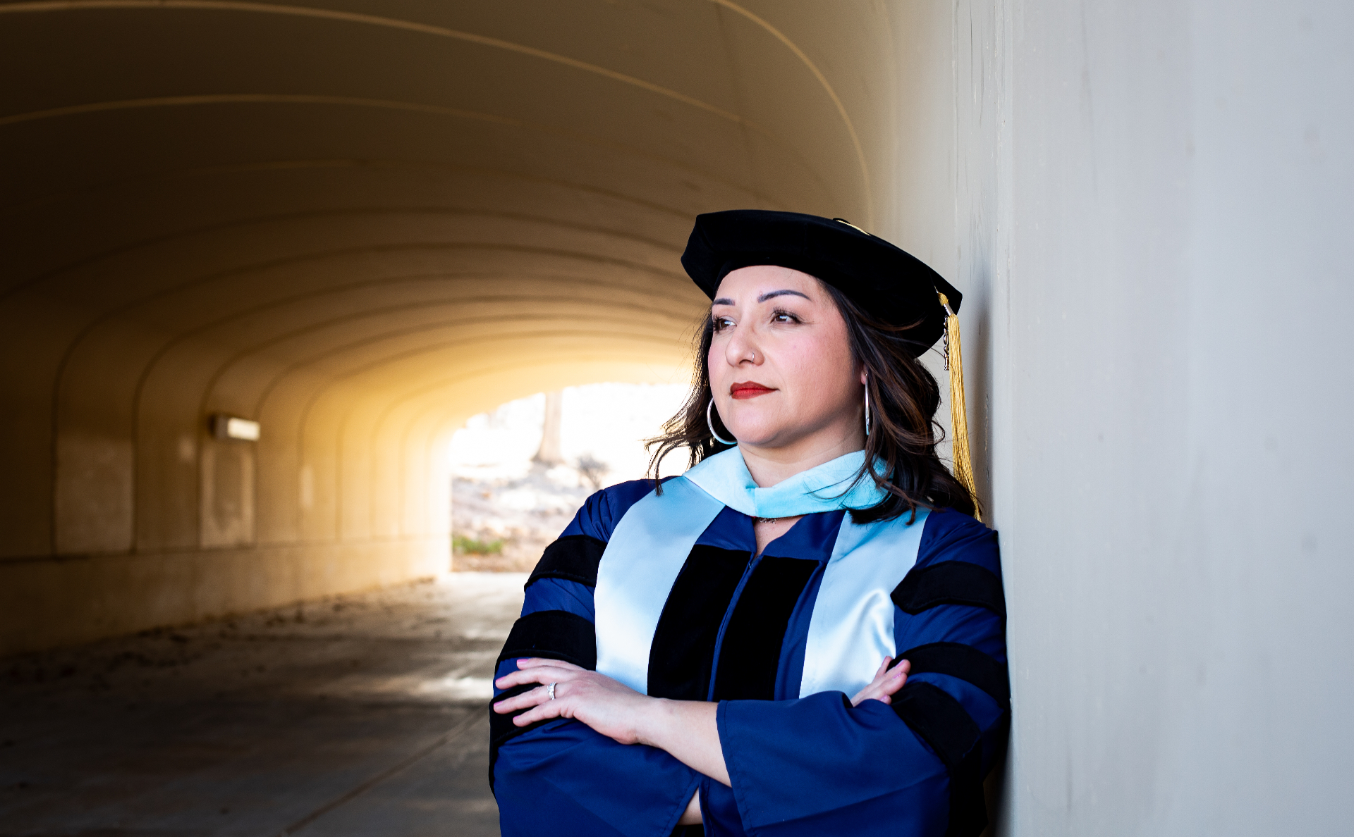 Dr. Martha A. Castillo in doctoral regalia, leaning against a wall